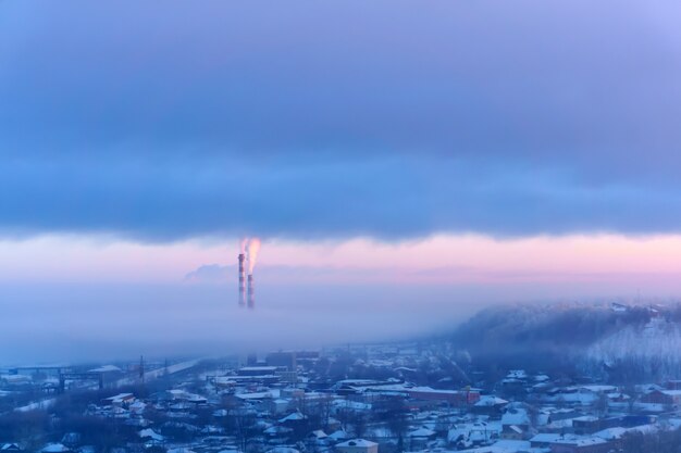 Paysage du soir d'une zone industrielle d'hiver avec cheminées fumantes et brume givrée