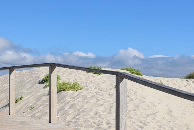 Paysage des dunes sur la plage de la mer Atlantique au Portugal avec du sable fin et blanc et une clôture en bois sur une journée d'été nuageuse