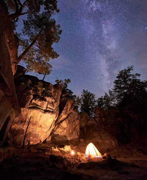 Paysage fantastique dans la nuit d'été. Petit feu de camp brûlant dans un canyon au milieu d'une énorme formation rocheuse escarpée sous un ciel étoilé sombre et clair. Concept de tourisme, de sécurité, d'escalade, de randonnée et de voyage.