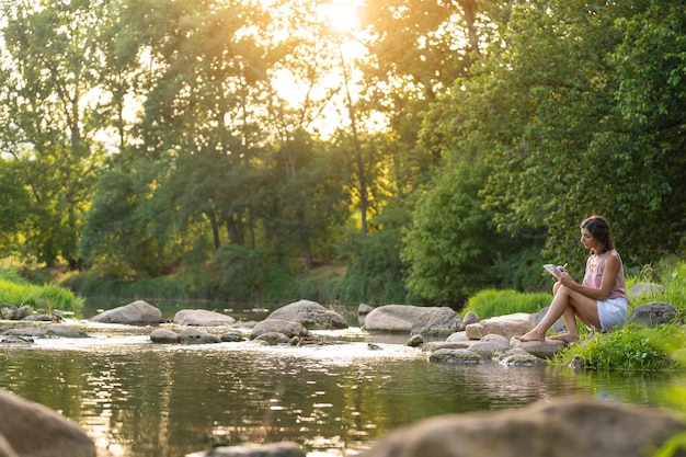 Photo paysage avec une femme qui lit près de la rivière au milieu de la nature