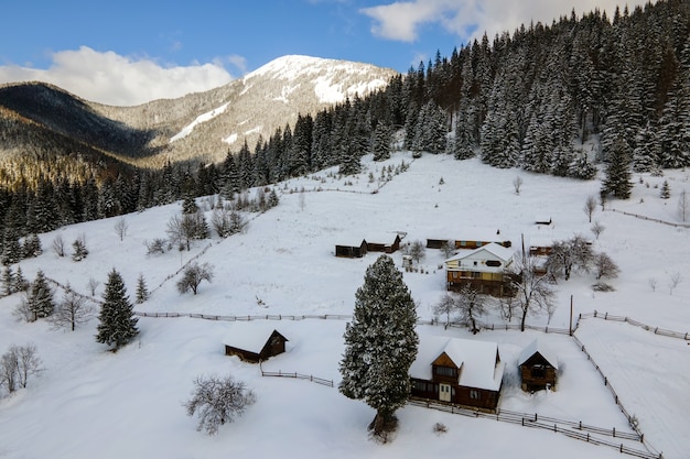 Paysage d'hiver aérien avec de petites maisons rurales entre la forêt couverte de neige dans les montagnes froides.