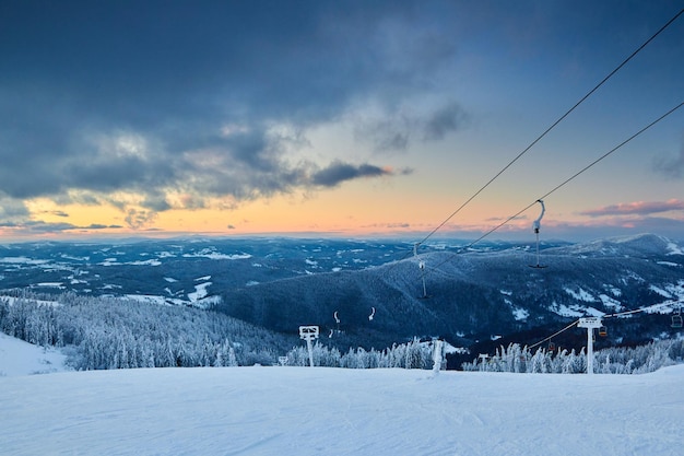 Paysage d'hiver du soir dans les montagnes avec forêt de sapins au coucher du soleil Collines couvertes de neige après de fortes chutes de neige Paysage de pistes de ski de l'arrière-pays enneigé Horizon de nuages dramatiques au lever du soleil