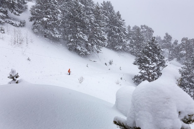 Paysage d'hiver avec une femme en veste lumineuse marchant le long d'une pente de montagne enneigée dans de fortes chutes de neige