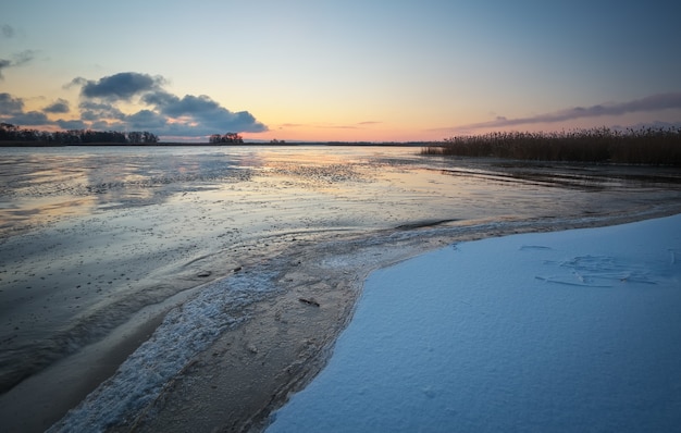 Paysage d'hiver avec lac gelé et ciel coucher de soleil. Ciel orange coloré. Composition de la nature.