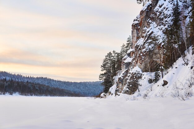 Paysage d'hiver avec une large rivière gelée dans une vallée boisée enneigée avec de hautes falaises calcaires