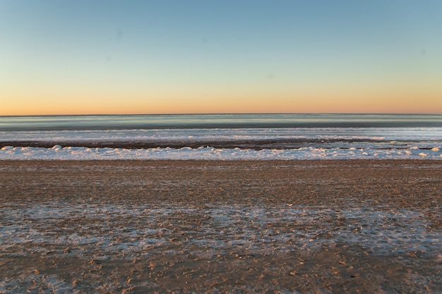 Paysage d'hiver en plage, littoral avec glace fissurée et eau de mer ouverte.