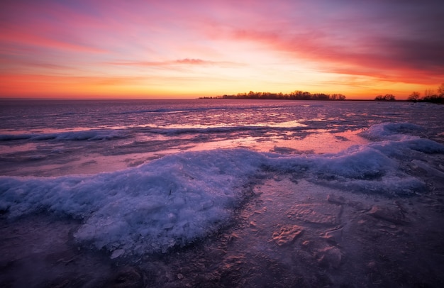 Paysage d'hiver avec rivière gelée et ciel de feu au coucher du soleil.