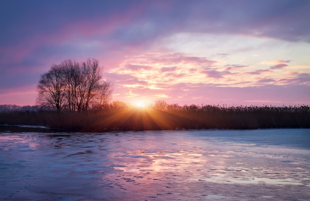 Paysage d'hiver avec soleil levant et rivière gelée.