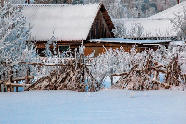 Paysage d'hiver une vieille maison en bois avec une clôture décrépite et branlante