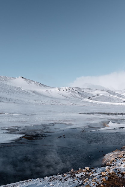 Photo paysage en islande avec lac geyser et route qui se perd dans la montagne enneigée