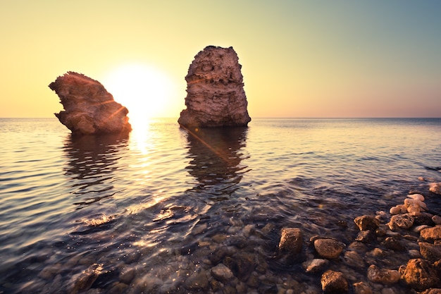 Paysage marin du rivage des eaux de mer immobiles, du fond pierreux et des rochers en mer au coucher du soleil