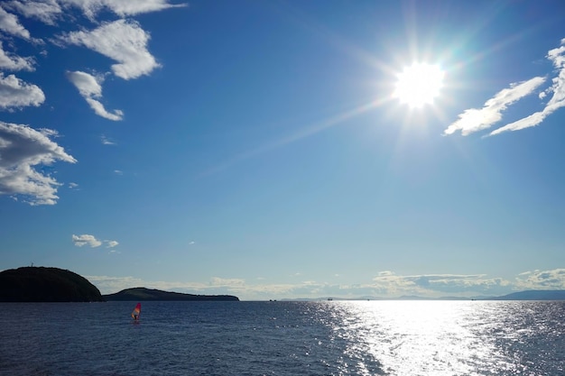 Un paysage marin avec un soleil éclatant et un surfeur sous une voile rouge