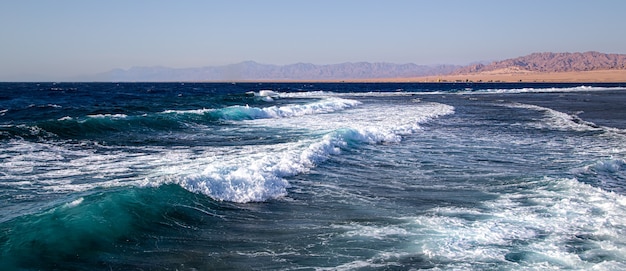 Paysage marin avec des vagues texturées et des silhouettes de montagne à l'horizon.