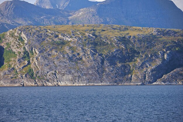 Le paysage d'une mer calme près d'une montagne rocheuse Une gamme de collines montagneuses verdoyantes au bord d'un grand lac en Norvège Océan paisible dans un littoral sauvage d'une scène de nature nordique pour l'espace de copie