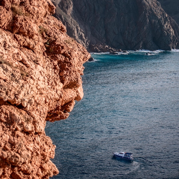 Paysage mer rochers montagnes et un petit bateau sur les vagues à l'arrière-plan il y a une ancienne forteresse