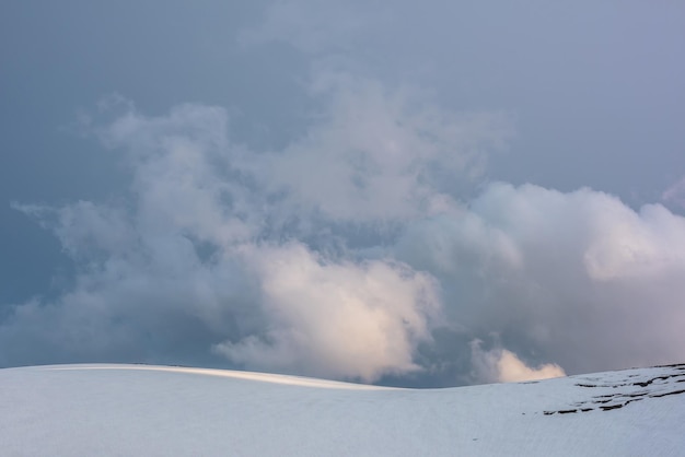 Paysage minimal dramatique avec un haut sommet de montagne enneigé ensoleillé sous un ciel nuageux au coucher du soleil Beau paysage alpin avec une grande montagne enneigée au soleil sous les nuages du soir par temps changeant