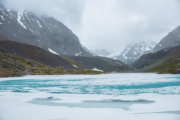 Paysage de montagne atmosphérique avec lac alpin gelé et hautes montagnes enneigées Superbe paysage couvert avec lac de montagne glacé sur fond de montagnes enneigées dans des nuages bas Vue panoramique sur le lac de glace