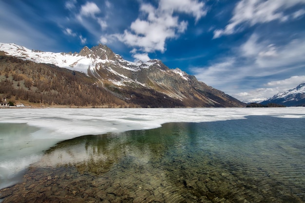 Paysage de montagne dans la vallée de l'Engadine avec un jeu de lumières au dégel du lac