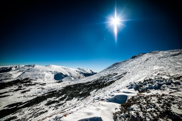 Un paysage de montagne enneigé avec un ciel bleu et un soleil qui brille sur les montagnes.