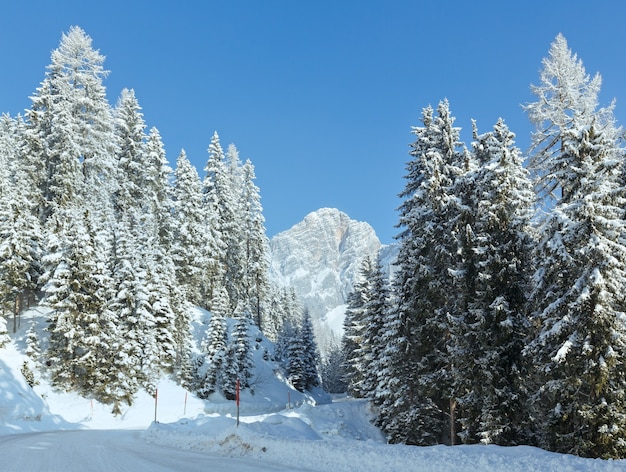 Paysage de montagne d'hiver du matin avec forêt de sapins et route de campagne sur la pente.