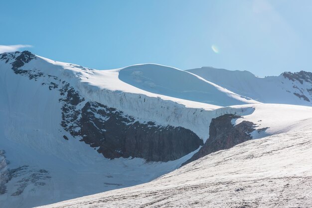 Paysage de montagne minimaliste avec un grand glacier au soleil Minimalisme enneigé simple avec langue glaciaire Vue alpine minimale sur les sommets des montagnes enneigées à très haute altitude sous un ciel bleu par temps ensoleillé