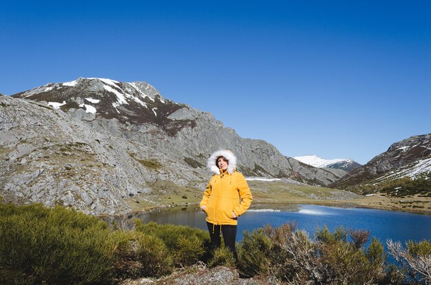 Paysage de montagne avec montagnes enneigées et lac. Femme en veste jaune regardant la caméra. Lac Isoba, Leon. Espagne.