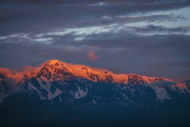 Paysage de montagne pittoresque avec de grandes montagnes enneigées éclairées par le soleil de l'aube parmi les nuages bas.