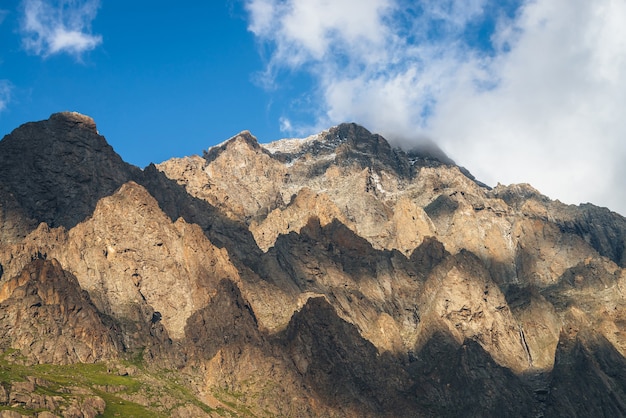 Paysage de montagne pittoresque avec de grands rochers au soleil doré et des nuages bas. Superbe paroi rocheuse avec un sommet pointu sous un soleil d'or. Paysage ensoleillé coloré avec une haute montagne rocheuse avec un pinacle pointu.