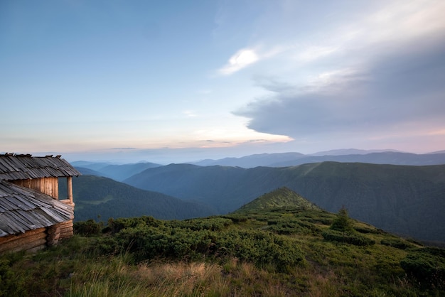 Paysage de montagne en soirée d'été avec un ancien abri touristique abandonné sur des collines herbeuses et des sommets lointains au coucher du soleil coloré