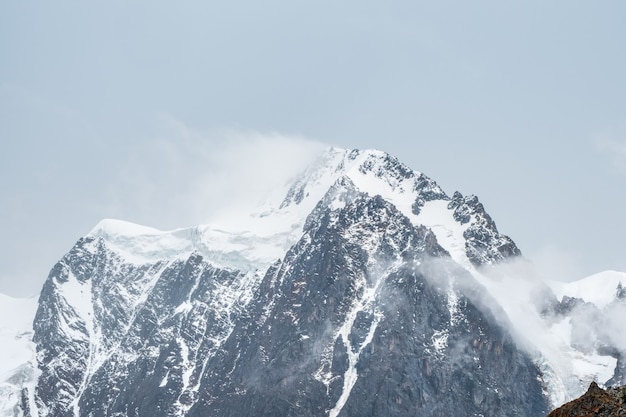 Paysage de montagnes atmosphériques hivernales avec blizzard au sommet d'une grande montagne enneigée dans les nuages bas. Superbe paysage minimal avec un glacier blanc sur des rochers noirs. Pinacle de haute montagne avec de la neige dans les nuages.