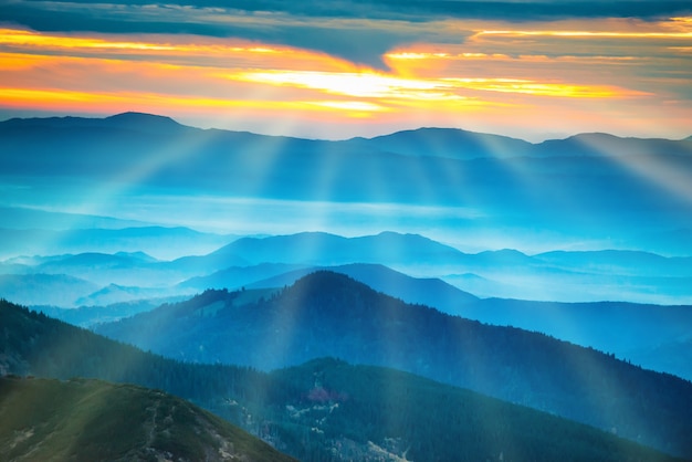 Paysage avec des montagnes bleues sous un beau coucher de soleil orange. La lumière du soleil et les rayons du soleil du ciel