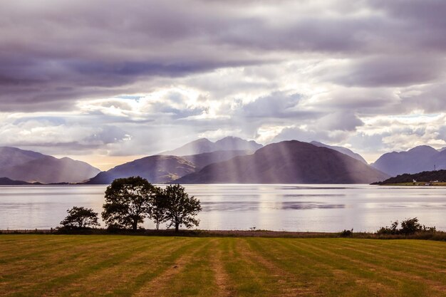 Paysage mystique paysage de lac en Ecosse ciel nuageux pré arbres et lac avec des rayons de soleil en arrière-plan Loch Linnhe