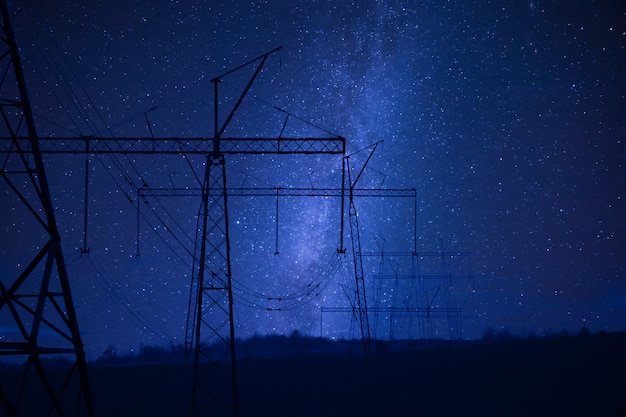 Paysage nocturne industriel avec ligne électrique à haute tension, tour électrique et étoiles un ciel