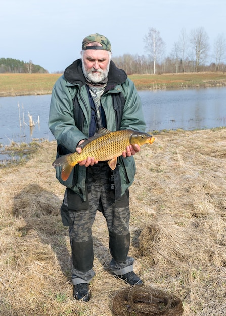 paysage avec un pêcheur sur le rivage d'une carpe de lac attrapée dans les mains d'un pêcheur amateur de carpe de pêche comme un passe-temps