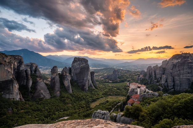 Paysage pittoresque au coucher du soleil d'une large vallée de montagne en Grèce avec des falaises bizarres, une forêt dense au pied des montagnes et un petit monastère chrétien au sommet d'une falaise