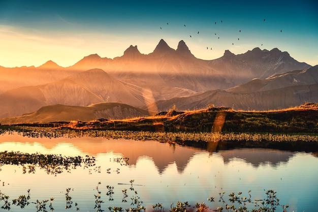 Photo paysage pittoresque du lever du soleil brille sur le lac guichard avec des oiseaux volant sur le massif d'arves et le reflet du lac en automne à aiguilles d'arves alpes françaises savoie france