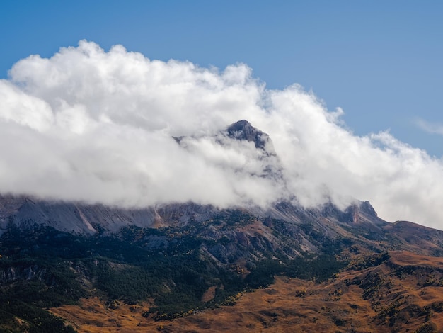 Paysage pittoresque avec vallée de montagne d'automne contre de grandes montagnes dans des nuages bas au soleil du matin Colline vive avec vue sur la chaîne de haute montagne du soleil dans des nuages bas