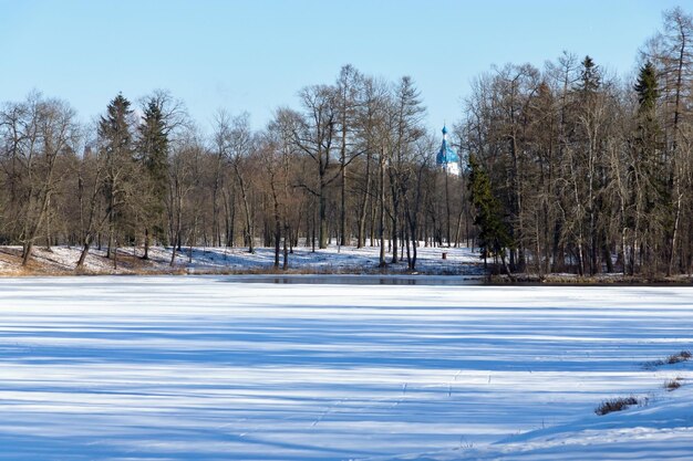 Paysage de printemps de la rivière gelée avec un patch dégelé et du bois avec une église sur fond