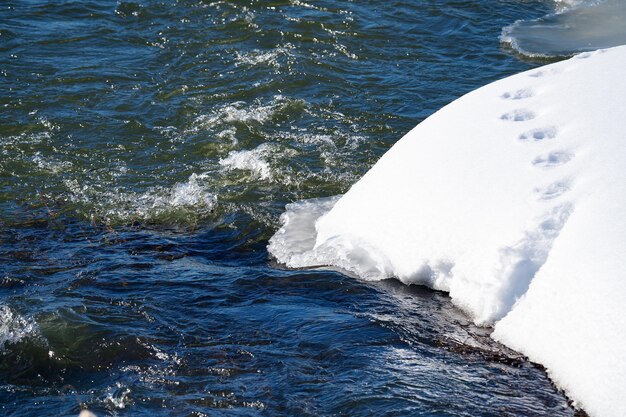 paysage de printemps avec une rivière sous la glace et des chutes de neige sur la rive