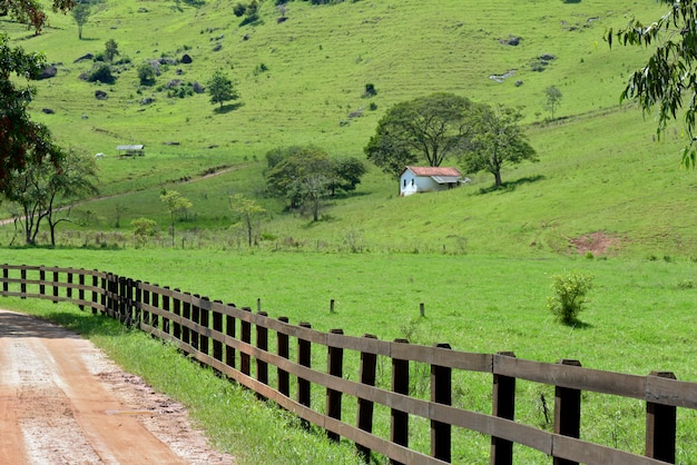 Paysage rural avec clôture au premier plan et petite maison en arrière-plan. Minas Gerai, Brésil