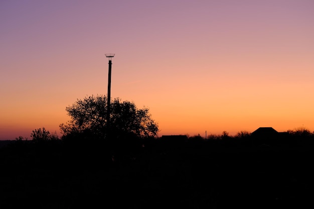 Paysage rural pittoresque bleu ciel coucher de soleil orange violet nuageux avec poteau et nid pour cigogne haute