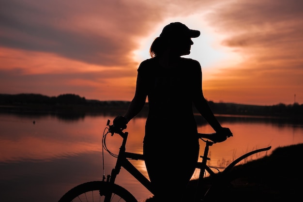 Paysage de silhouette d'été Fille avec un vélo au bord du lac sur fond de soleil couchant le coucher de soleil cramoisi