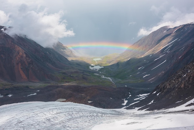 Photo paysage sombre avec un arc-en-ciel vif au-dessus du lac de montagne paysage sombre avec un arc-en-ciel brillant au-dessus du glacier et du lac glaciaire dans la vallée de montagne vue supérieure sur l'arc-en-ciel coloré et les nuages bas dans les montagnes