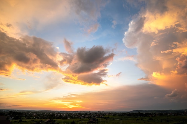 Paysage spectaculaire au coucher du soleil avec des nuages gonflés éclairés par un soleil couchant orange et un ciel bleu.