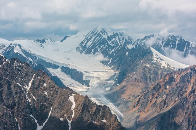 Paysage spectaculaire avec une longue langue glaciaire et de hautes montagnes enneigées sous un ciel nuageux Magnifique vue aérienne sur un grand glacier ensoleillé et un sommet enneigé dans les nuages Vue de dessus sur des montagnes majestueuses