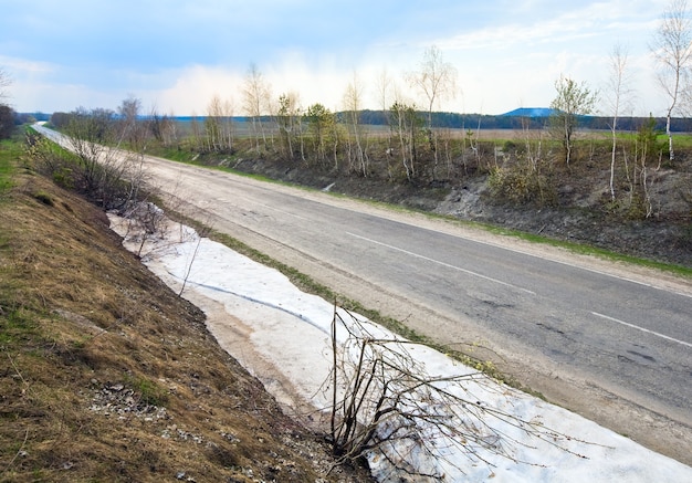 Photo paysage terne de printemps avec route de campagne et neige fondante à côté