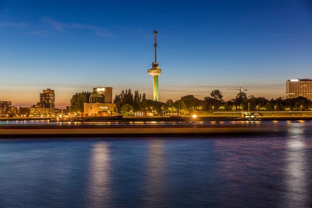 Photo paysage urbain nocturne de la nouvelle maas bâtiments éclairés par la rivière contre le ciel bleu euromast