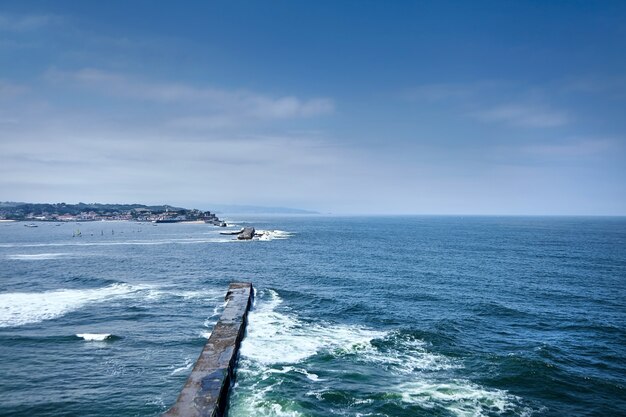 Paysage avec vagues de l'océan se brisant sur le barrage en pierre et vue sur la ville Château de Ciboure et port de Socoa