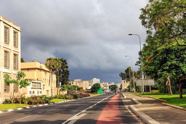 Paysage de la ville Des bâtiments et des arbres à fleurs vertes bordent la route menant en perspective Le matin avant un orage dans la ville de Haïfa, Israël