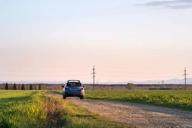 Paysage avec une voiture tout-terrain bleue sur une route de gravier.